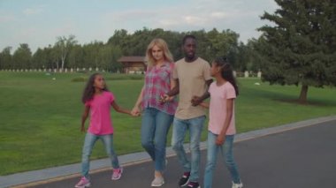 Çocukların parkta dinlendiği neşeli, çeşitli bir aile.