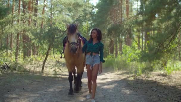 Pečující jezdkyně vedoucí koně na lesní stezce — Stock video