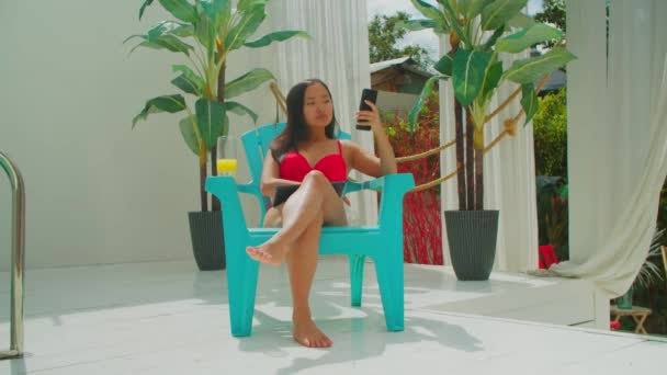 Sourire asiatique fille avec smartphone repos par piscine — Video