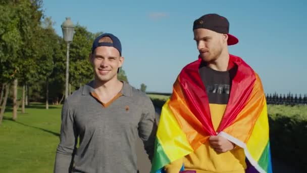 Twee mannelijke minnaars met trotse vlag wandelen in het park — Stockvideo