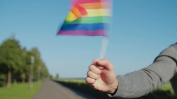 Крупним планом чоловіча рука махає веселкою прапор на відкритому повітрі — стокове відео