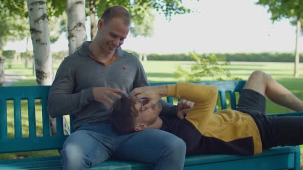 Szczęśliwy gej leżący na chłopaki okrążenie na park ławka — Wideo stockowe