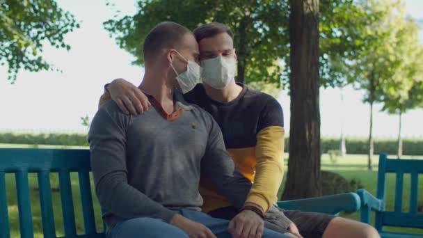 Romantisch gay paar in gezicht maskers zitten op bank — Stockvideo