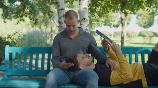 Gay paar ontspannen met digitale apparaten buiten — Stockvideo