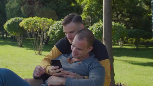 Felici amanti dello stesso sesso che condividono smartphone nel parco — Video Stock