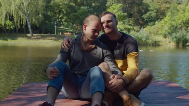Loving gay couple resting on wooden pier by lake — Stock Video
