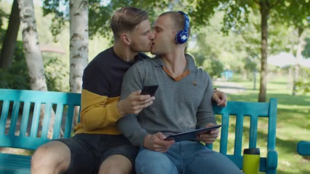 Fröhliches schwules Paar mit Gadgets entspannt sich im Park — Stockvideo