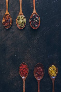 Eski siyah masada tahta kaşıklarda çeşitli baharatlar.
