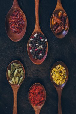 Eski siyah masada tahta kaşıklarda çeşitli baharatlar.