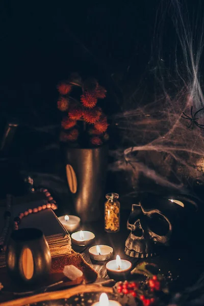 Eine rituelle Halloween-Hexerei-Szene mit Kerzen, Kräutern, Spinnennetz, Vintage-Flaschen auf rustikalem Hintergrund mit gruseligem Totenkopf-Gesicht und antikem Buch — Stockfoto