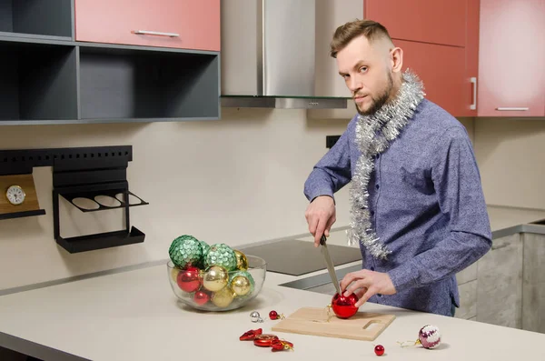 Young attractive bearded man with knife in his hand cuts salad of decorated Christmas balls. Concept of preparation for the holiday. toned.