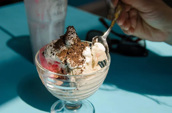 female hand with a spoon is picking ice cream from a glass bowl