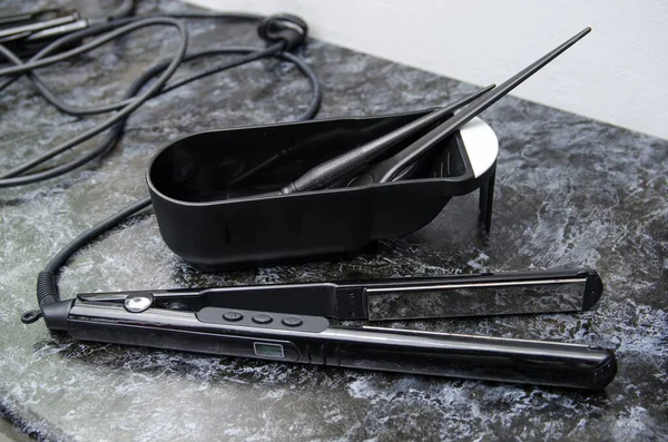 plastic black brushes for dyeing hair in an empty container for paint and curling tongs on the board.