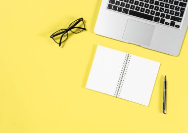 Office çalışma alanı en az düz yatıyordu. Laptop, defter, sarı zemin üzerine gözlük