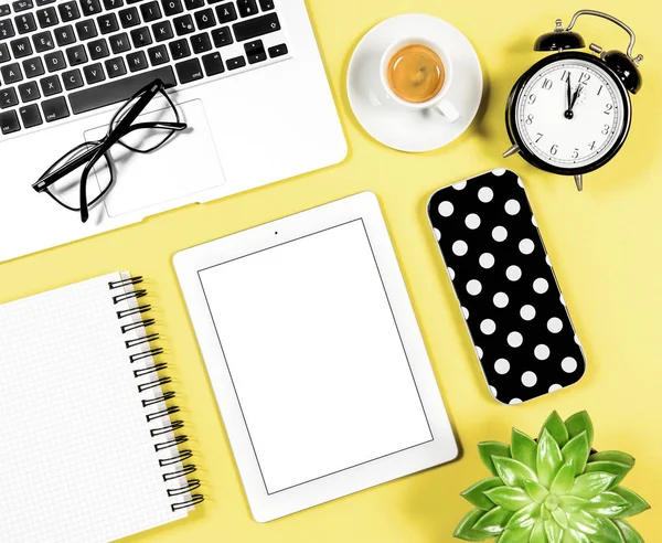 Flat lay office workplace. Laptop, notebook, tablet PC, coffee, succulent plant, alarm clock on yellow background