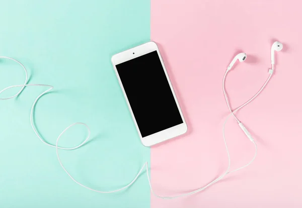 Mobile phone with headphones on pink blue background. Minimal flat lay