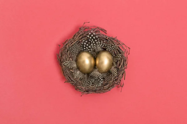 金色的复活节彩蛋在鸟巢珊瑚粉红色的背景 最小平面铺设 — 图库照片