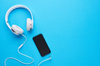 Kopya alanı ile mavi arka plan üzerinde en iyi görünümü siyah cep telefonu ve beyaz kulaklık. Düz yatıyordu.