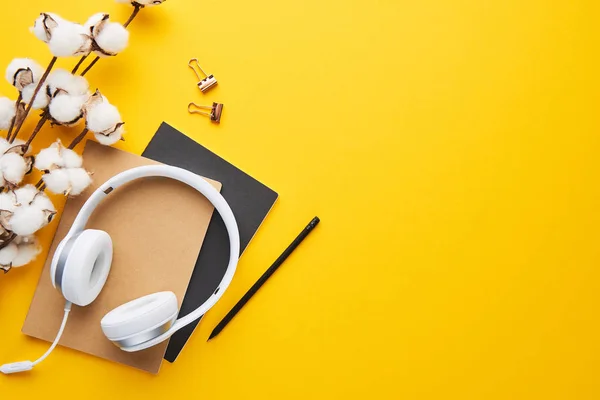 Top view of white headphones, notebooks and cotton on yellow background with copy space. Flat lay.