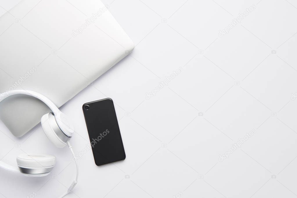 Minimal work space concept. Top view of laptop, white headphones and black cell phone on white background with copy space. Flat lay.