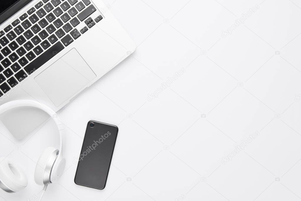 Minimal work space concept. Top view of laptop, white headphones and black cell phone on white background with copy space. Flat lay.