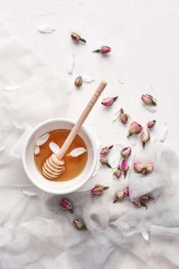 Düz bal küçük seramik kase, ahşap bal ayı, ipek, yaprakları ve kuru gül beyaz bir arka plan üzerinde kopya alanı ile yatıyordu. Üstten görünüm.