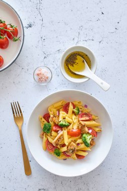 İtalyan yemeği. Düdük makarna salatası ile İtalyan soyunma yatıyordu düz, domates, brokoli ve fesleğen yaprakları beyaz mermer zemin üzerine. Üstten görünüm.