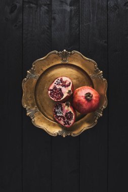 Düz olgun nar meyve bir eski altın hizmet plaka, siyah ahşap antika arka plan üzerinde yatıyordu. Kopya alanı ile üstten görünüm.