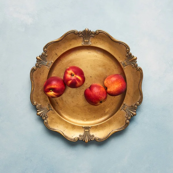 Düz taze nektarin meyve üzerinde açık mavi renkli rustik altın servis tabağı üzerinde yatıyordu. Üstten görünüm, kare kırpma.