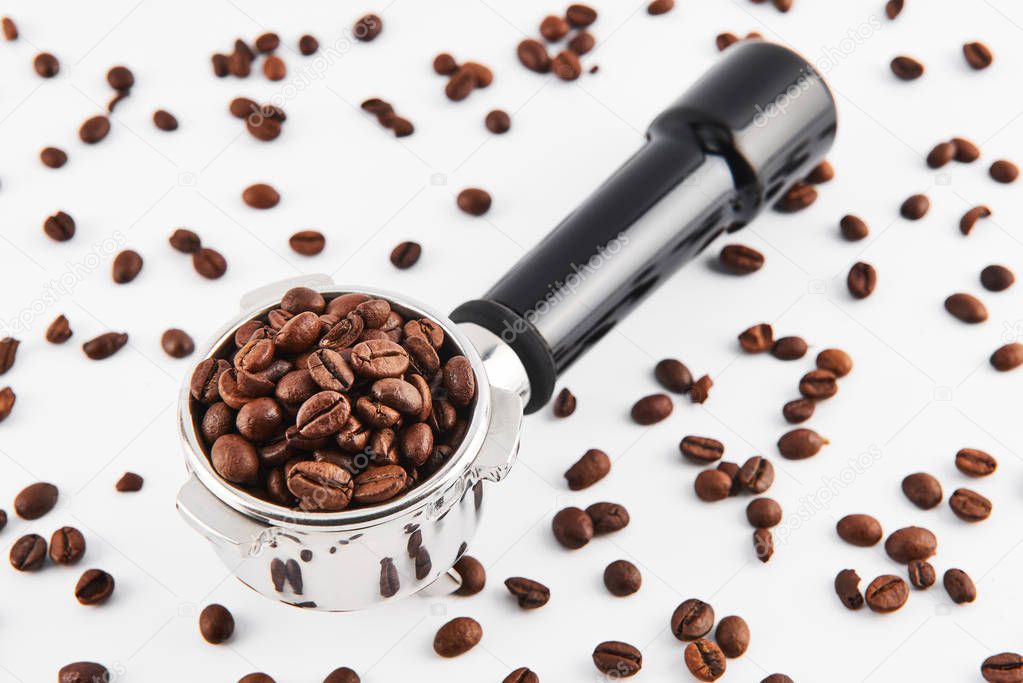 Portafilter filled and surrounded with whole coffee beans isolated on white background. Filter holder for espresso coffee machine.