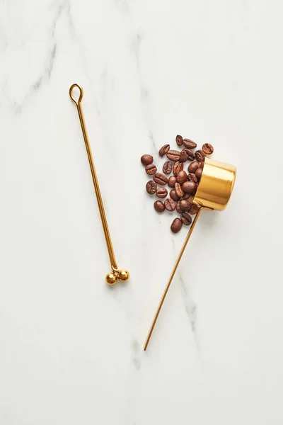 Concept of coffee accessories. Flat lay of golden clip and scoop with coffee beans on marble background. Top view.