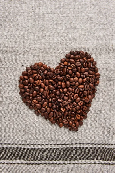 Heart from coffee beans on a beige dish towel background. Flat lay with copy space.