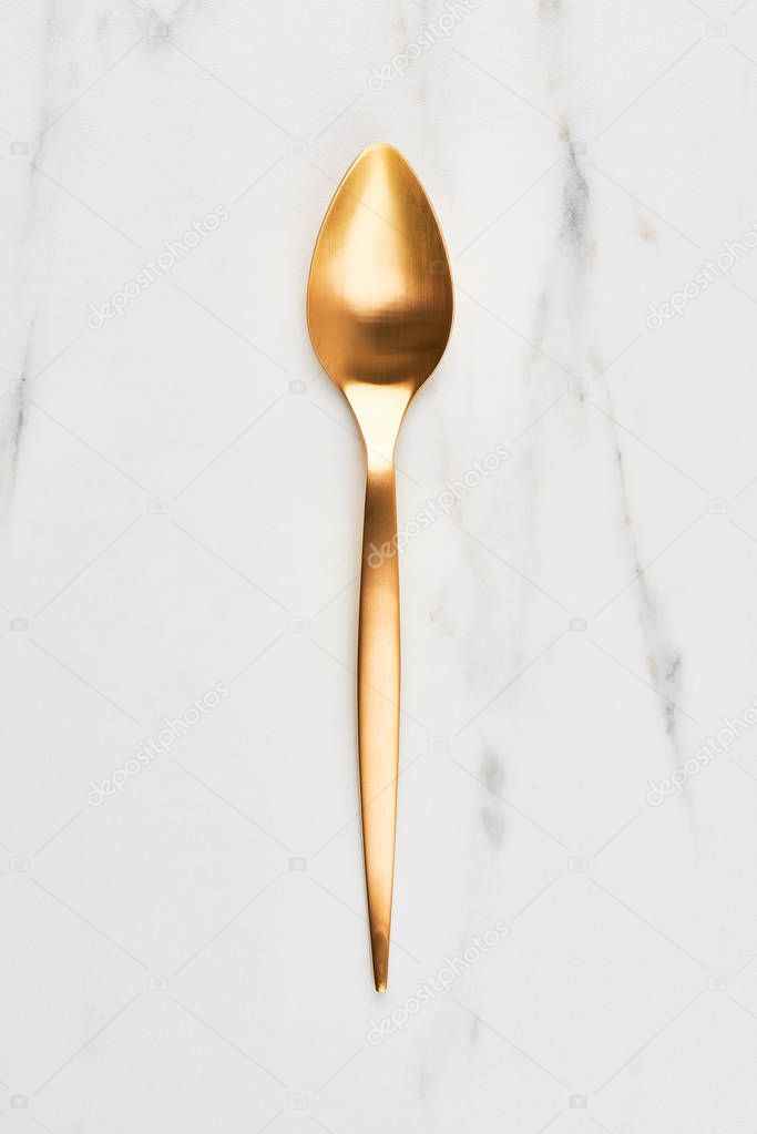 Flat lay of golden spoon on white marble background. Top view, high resolution image.