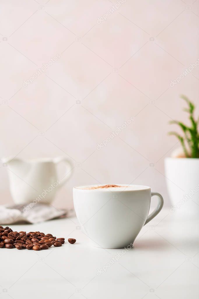 Cappuccino in a white ceramic coffee cup with roasted coffee beans. Feminine rose background with copy space. High resolution image, narrow depth of field.
