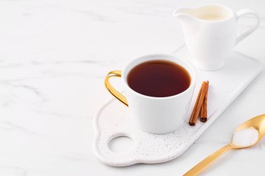 Servis tabağı üzerinde çay, tarçın ve süt kabı, altın kaşık şekerle beyaz mermer masa kopya alanı ile üstü ile beyaz fincan. Dar alan derinliği.