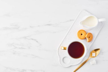 «Ana sayfa» plaka, kesme şeker beyaz mermer zemin üzerine altın kaşıkla hizmet üzerinde beyaz fincan çay, kurabiye ve süt kabı görünümünü. Düz kopya alanı ile yatıyordu.