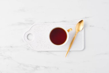 Beyaz fincan çay altın kaşıkla üstten görünüm üzerinde noktalı servis tabağı. Fincan çay beyaz mermer zemin üzerinde. Düz kopya alanı ile yatıyordu.