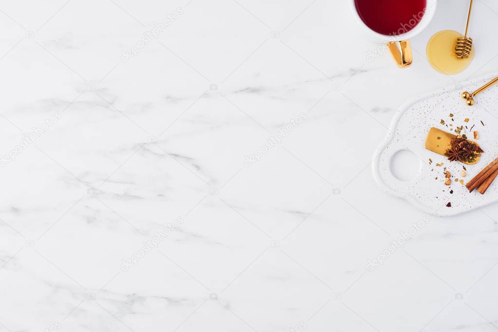 Top view of white cup of tea, golden spoon, herbs and tea mesure on serving plate. Cup of tea on white marble background with dried herbs. Flat lay.