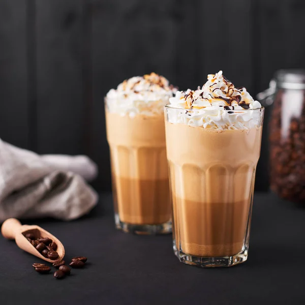 Buzlu latte kahve karamel ve çikolata şurubu ve krem şanti ile uzun bir bardak. Koyu ahşap arka plan.