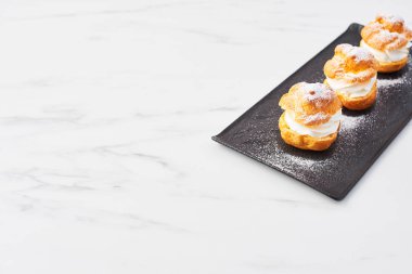 Beyaz mermer masa üzerinde siyah bir tabakta üstten görünüm lezzetli krem puf kek krem ve pudra şekeri ile. Seçici odak, kopya alanı.