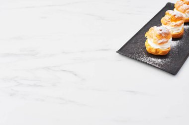 Beyaz mermer masa üzerinde siyah bir tabakta üstten görünüm lezzetli krem puf kek krem ve pudra şekeri ile. Seçici odak, kopya alanı.