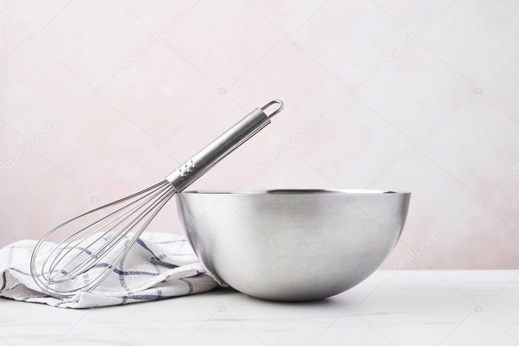 Baking concept. Bowl with a whisk and dishcloth on white marble table over pink background with copy space.