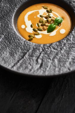 Kabak çekirdeği, krem ve siyah modern plaka üzerinde kopya alanı ile koyu ahşap masa fesleğen ile kabak ve havuç çorbası kapatın. Üstten görünüm.