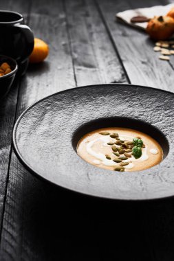 Kabak çekirdeği, krem ve siyah modern plaka üzerinde kopya alanı ile koyu ahşap masa fesleğen ile kabak ve havuç çorbası. Karanlık modern tarzı.