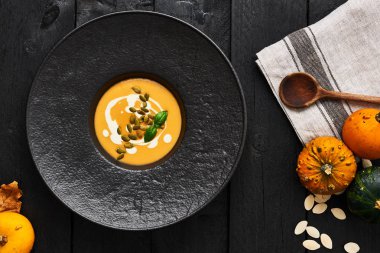Kabak çekirdeği, krema ve koyu ahşap arka plan üzerinde siyah modern plaka fesleğen ile kabak ve havuç çorbası. Üstten görünüm.
