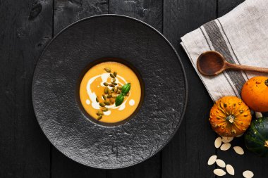 Kabak çekirdeği, krema ve koyu ahşap arka plan üzerinde fesleğen ile kabak ve havuç çorbası. Üstten görünüm.