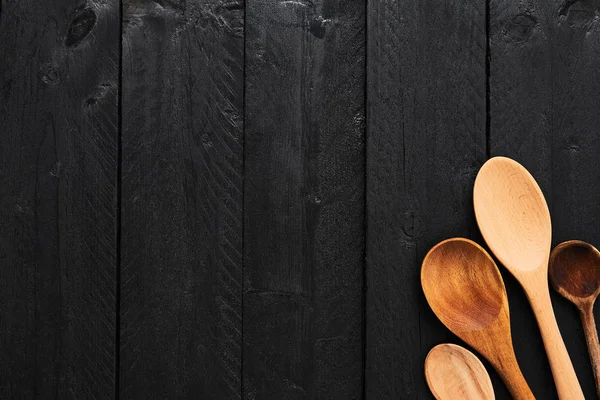 Wooden spoons on black wooden background with copy space. Top view of various types of wooden spoons on dark wooden background.