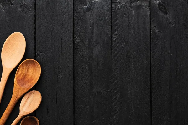 Wooden spoons on black wooden background with copy space. A collection of wooden kitchen utensils on dark wooden background. Top view.