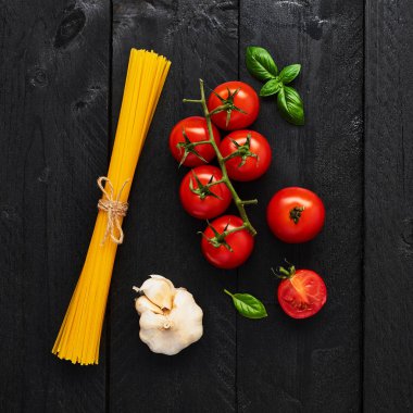 Spagetti, domates sarımsak ve fesleğen ile lezzetli İtalyan yemekleri için gıda arka plan. Çeşitli pişirme malzemelerin üzerine siyah ahşap masa. Üstten görünüm.
