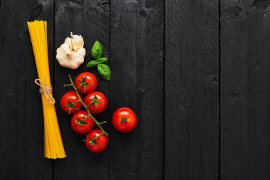 Spagetti, domates sarımsak ve fesleğen ile lezzetli İtalyan yemekleri için gıda arka plan. Çeşitli pişirme malzemelerin üzerine siyah ahşap masa. Kopya alanı ile üstten görünüm.